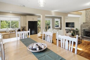 A spacious kitchen with white cabinetry, a dining table with chairs, and a fireplace. - Cedar Barrel Lakehouse - Hot Tub|Water Toys|Views (Kawartha Lakes)