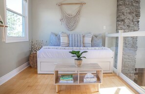 A bedroom with a bed, a hanging macrame chair, a bedside table with books, and a stone wall. - Cedar Barrel Lakehouse - Hot Tub|Water Toys|Views (Kawartha Lakes)