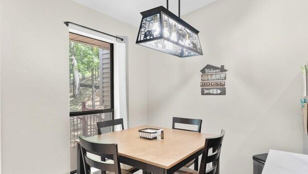 A dining area with a table, chairs, a hanging light fixture, and a window with blinds. - Timber and Trail  2BR/2BA Family Friendly (Kimberling City)