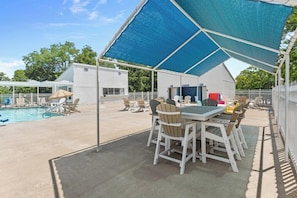 Um pátio externo com piscina, área de estar coberta e uma mesa com cadeiras.