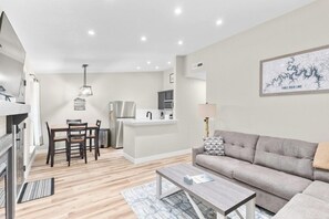 A modern living room with a sofa, coffee table, and dining area with chairs. - Timber and Trail  2BR/2BA Family Friendly (Kimberling City)