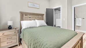 A bedroom with a wooden bed, a nightstand with a lamp, a framed quote on the wall, and a door leading to a bathroom. - Timber and Trail  2BR/2BA Family Friendly (Kimberling City)