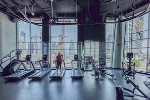 Ein Fitnessstudio mit Laufbändern, Crosstrainern und Krafttrainingsgeräten, mit großen Fenstern und Blick auf die Stadt.
