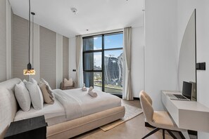 Ein modernes Hotelzimmer mit einem großen Bett, einem Schreibtisch, einem Stuhl und Blick auf eine Skyline durch große Fenster.