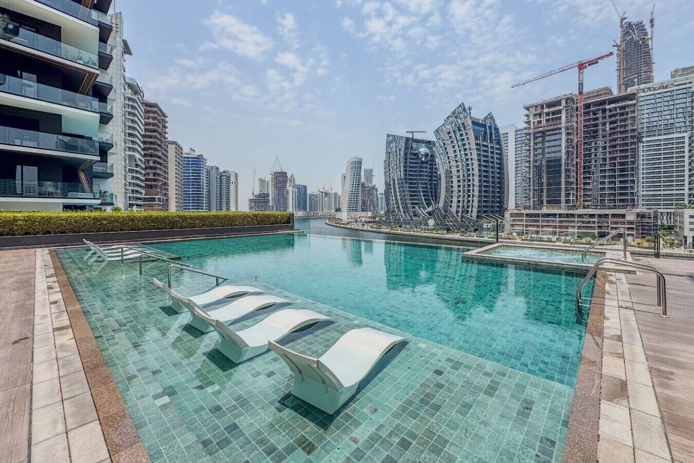 Piscina com água cristalina, cercada por edif ícios modernos e guindastes de construção, sinalizando uma área em desenvolvimento urbano.