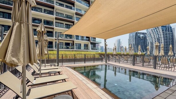 Ein Pool auf dem Dach mit Liegestühlen und Sonnenschirmen, umgeben von Hochhäusern.