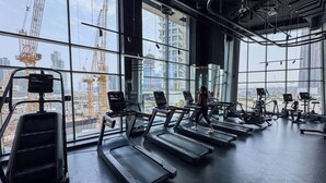 Ein Fitnessstudio mit Laufbändern und Trainingsgeräten, große Fenster mit Blick auf die Stadt und sichtbare Baukräne draußen.