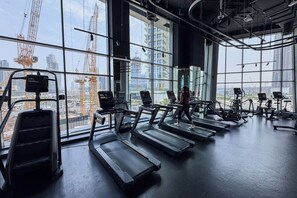Ein Fitnessstudio mit Laufbändern und Trainingsgeräten, große Fenster mit Blick auf die Stadt und sichtbare Baukräne draußen.