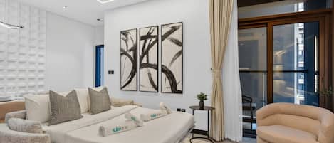 Une chambre d’hôtel moderne avec un lit, un canapé, une table ronde et une œuvre d’art abstraite au mur.