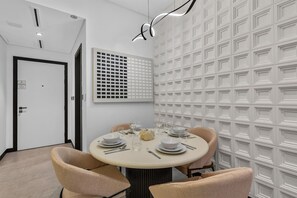 Ein Essbereich mit einem runden Tisch, gedeckt für vier Personen, umgeben von Stühlen, in einem Raum mit einem Wandmuster und einer Tür im Hintergrund.