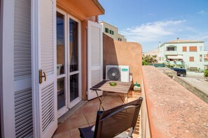 Ein Balkon mit Tisch, Stuhl, einem Ventilator und einem Fenster mit Rollläden.