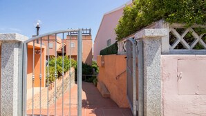 A gated entrance to a residential area with a clear pathway leading to a building with a pink facade. - GuestHost - Palau Comfy Flat with Balcony (Palau)