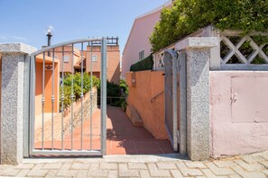 Ein verschlossenes Tor zu einem Wohngebiet, mit einem deutlichen Weg, der zu einem Gebäude mit rosa Fassade führt.