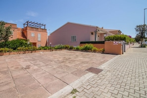 Ein Wohngebiet mit einem gepflasterten Innenhof, einem pinkfarbenen Gebäude mit einer Pergola und einem verschlossenen Eingang.