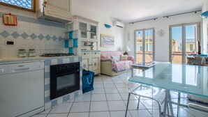 A kitchen with a dishwasher, stove, and cabinets, a glass table, and a window with a view. - GuestHost - Palau Comfy Flat with Balcony (Palau)