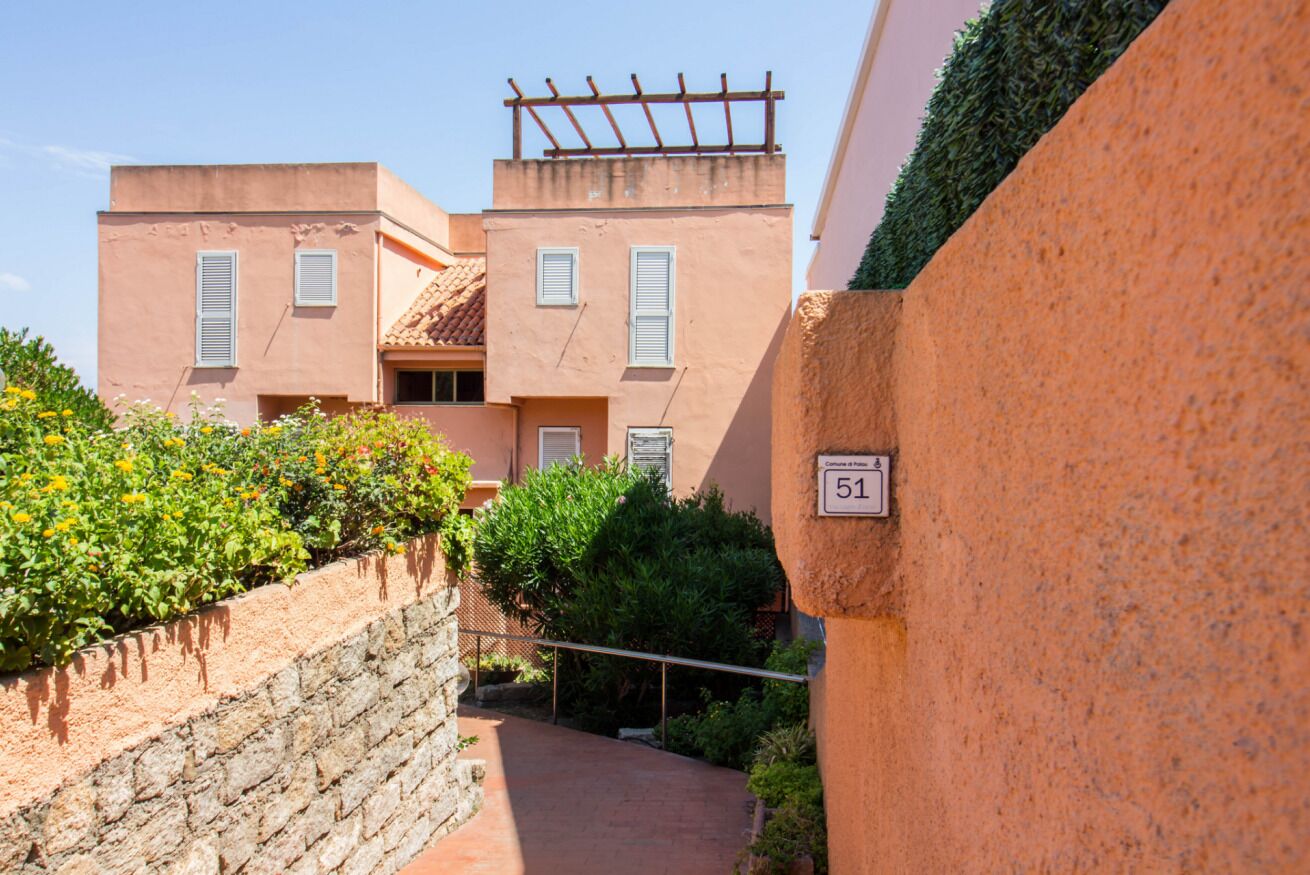 A narrow stone pathway leading to a building with a number 51 sign, surrounded by greenery and a stone wall.