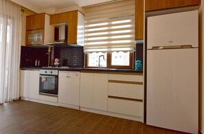A kitchen with wooden cabinets, a built-in oven, a dishwasher, and a refrigerator. - Inanlar Airport Residence  (Ortahisar)