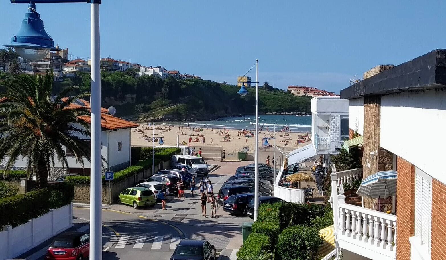 A coastal street with parked cars, a pedestrian crossing, and a beach in the background.