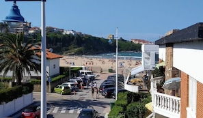 A coastal street with parked cars, a pedestrian crossing, and a beach in the background.