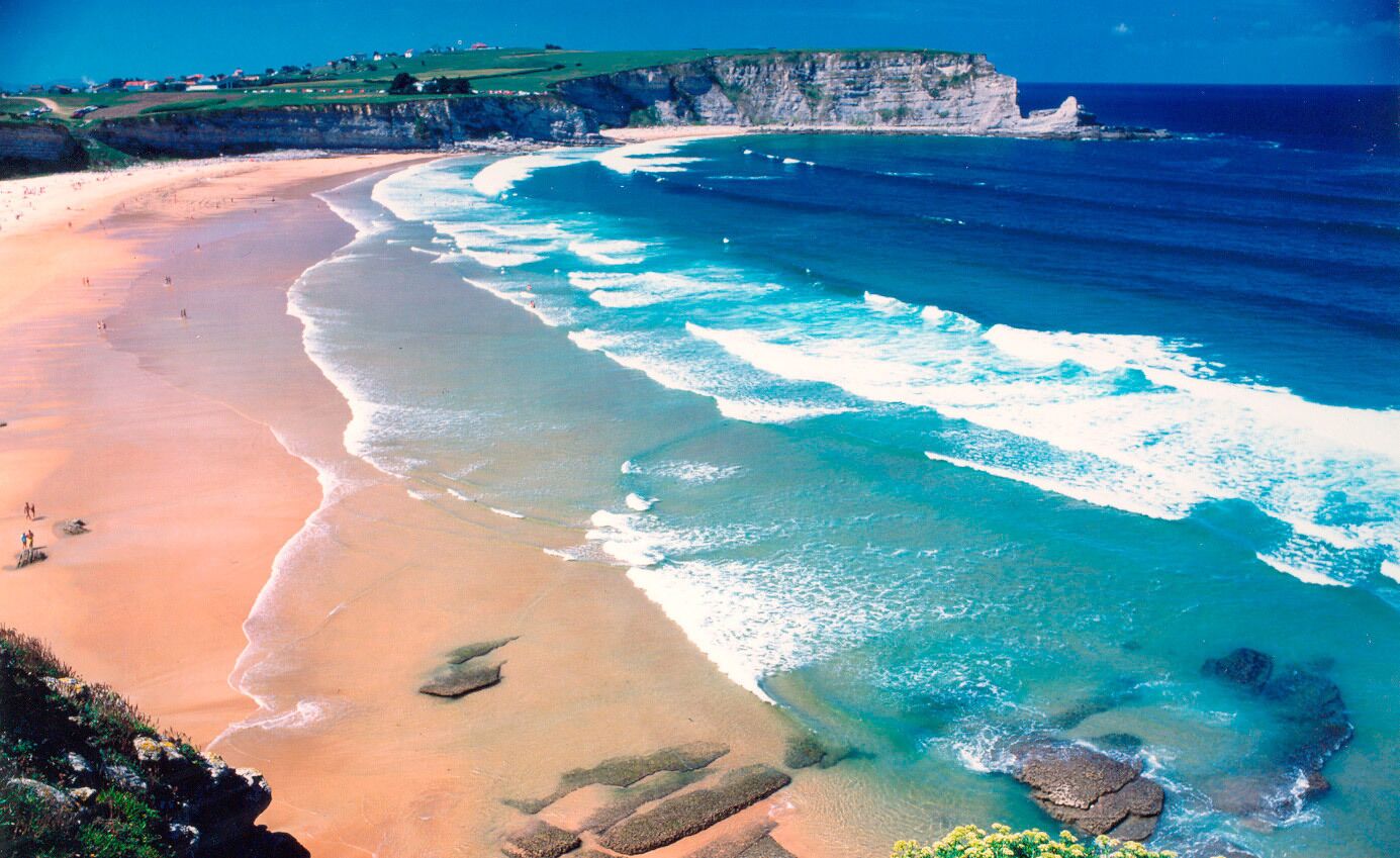 A coastal beach with clear waters, a sandy shore, and rocky outcrops.