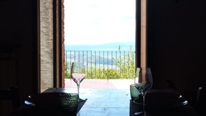 Un'apertura che dà su una terrazza con tavolo e sedie, con vista su un paesaggio che include una recinzione e dolci colline in lontananza.