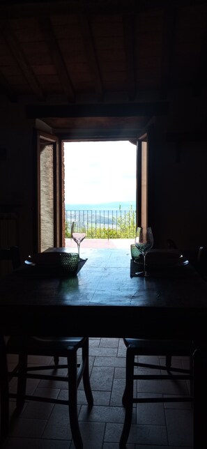 An open doorway leading to a terrace with a table and chairs, overlooking a landscape with a fence and distant hills. - Cozy Studio Apartment in the Tuscan Countryside (Seggiano)