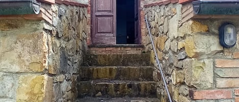 Une série de marches en pierre menant à une porte en bois, agrémentée d’une rampe métallique.