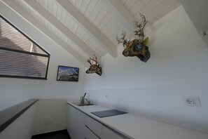 A kitchen with white cabinets, a black countertop, a window with blinds, and wall-mounted deer antlers. - Cirasa Luxury Country House (Trecastagni)