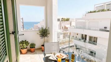A balcony with a table set for breakfast, potted plants, and a view of the sea and buildings.