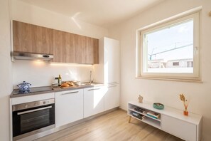 Eine moderne Küche mit weißen Schränken, einem eingebauten Ofen, einer Edelstahl-Dunstabzugshaube und einem Fenster für natürliches Licht.