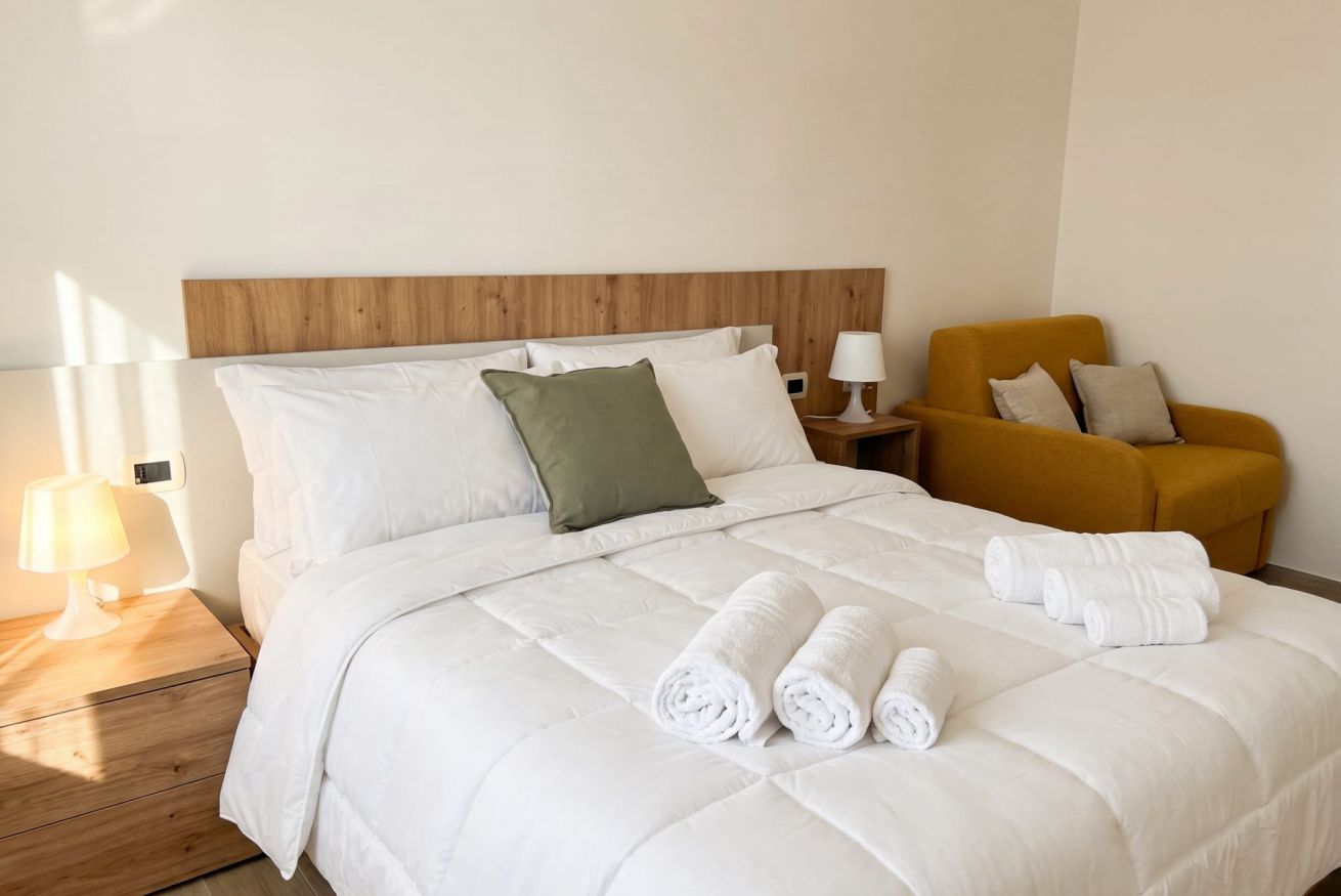 A hotel room with a bed, pillows, a nightstand, a lamp, and a chair.