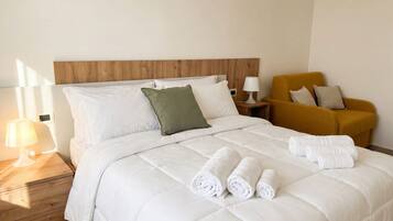 A hotel room with a bed, pillows, a nightstand, a lamp, and a chair.