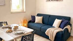 Ein Essbereich mit einem für zwei Personen gedecktem Tisch, einem blauen Sofa und einem an der Wand befestigten Kalender.