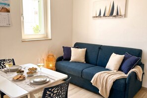 Ein Essbereich mit einem für zwei Personen gedecktem Tisch, einem blauen Sofa und einem an der Wand befestigten Kalender.