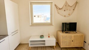 Ein Zimmer mit einem weißen Schrank, einem Fernseher darauf, einem kleinen Tisch mit Schüssel und Vase sowie einem Fenster mit Blick auf Gebäude.