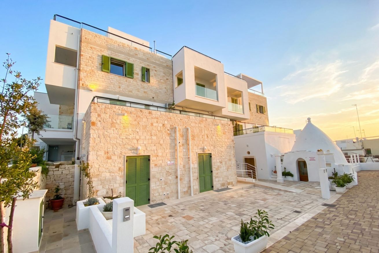 A modern building with a stone facade, multiple balconies, and a courtyard with potted plants.
