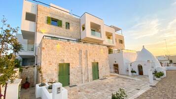 A modern building with a stone facade, multiple balconies, and a courtyard with potted plants.