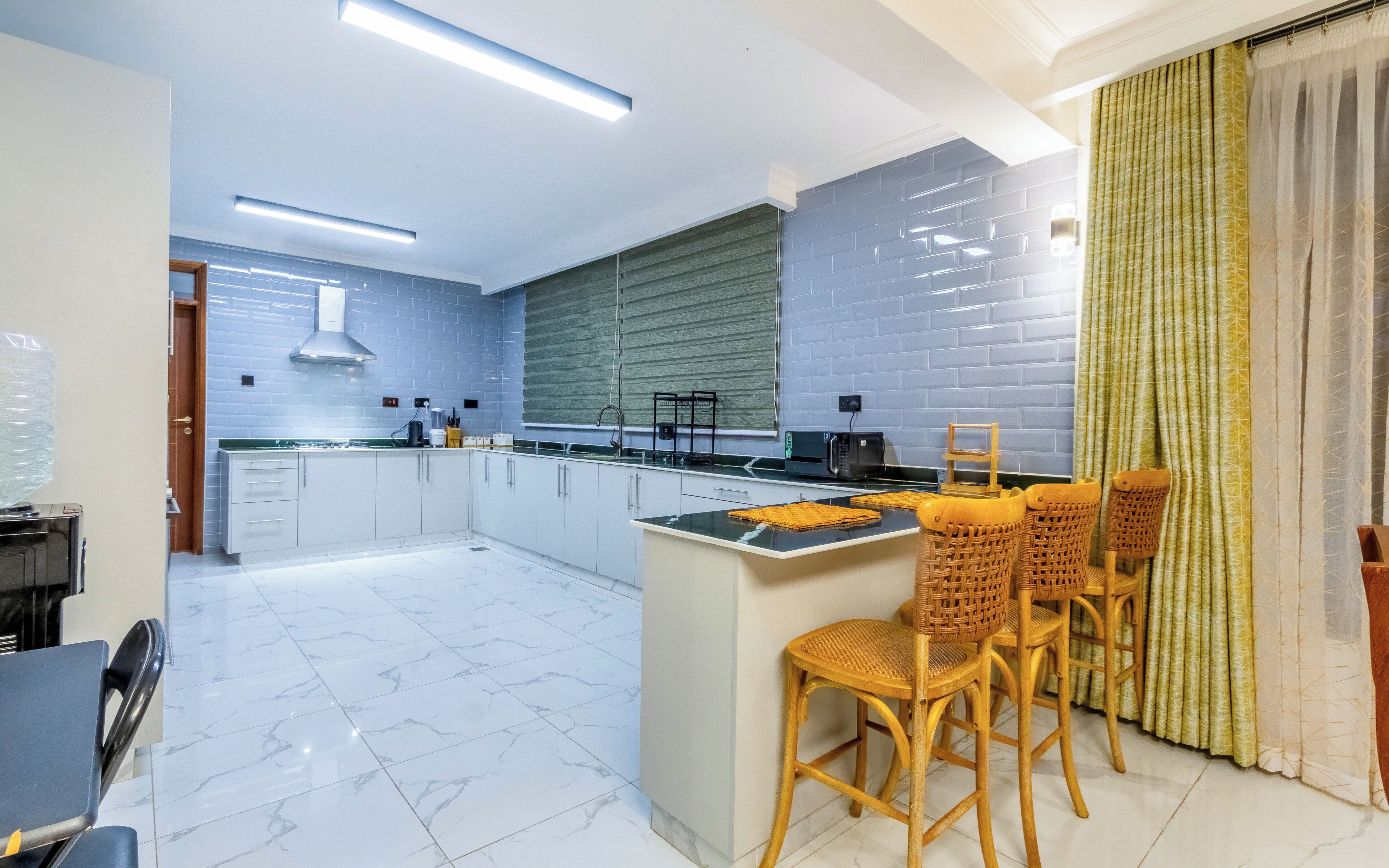 A modern kitchen with white cabinets, a marble floor, and a dining area with wicker chairs.