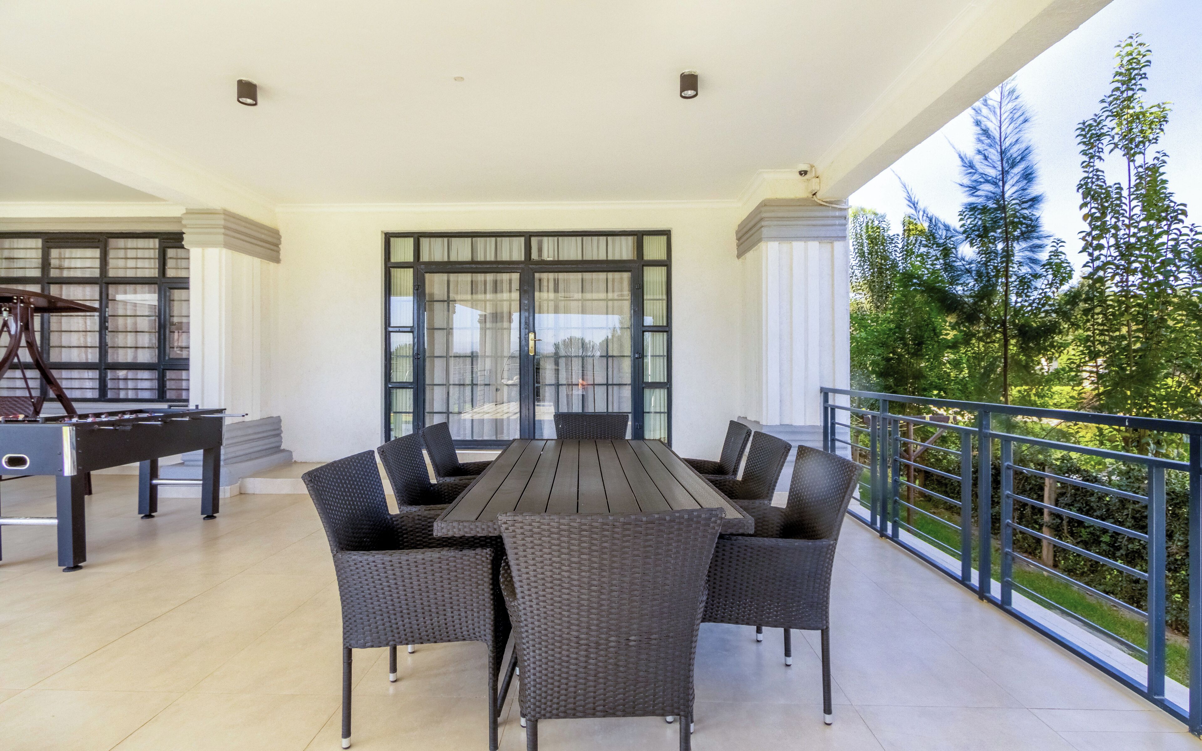 Portico coperto con tavolo e sedie da pranzo, un pianoforte e vista su piante.