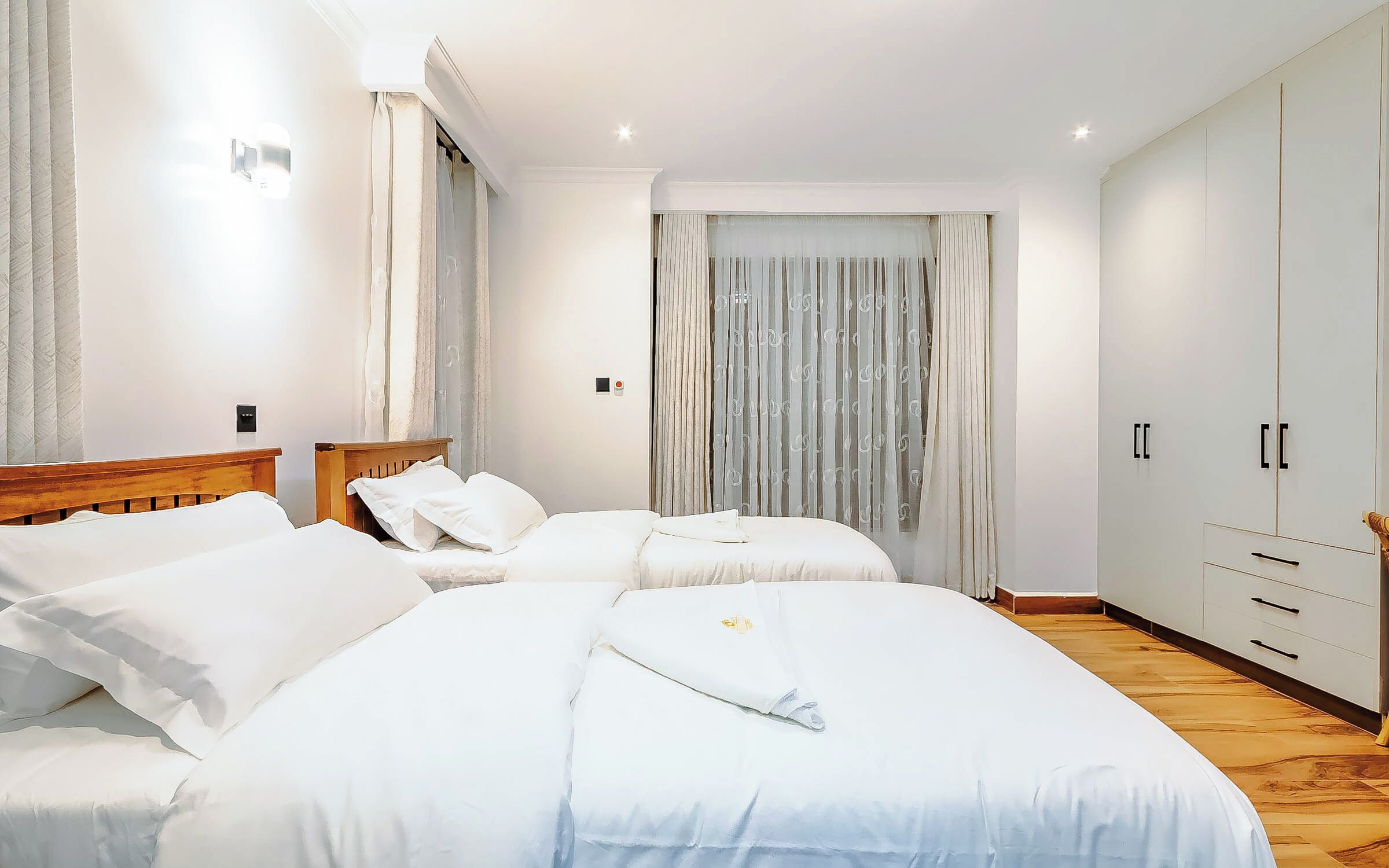 A bedroom with two beds, a wardrobe, and a window with curtains.
