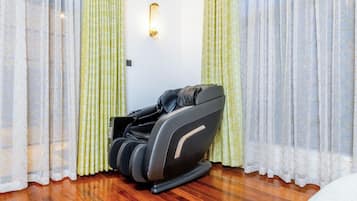 Uma cadeira de massagem em um quarto com piso de madeira e cortinas estampadas.