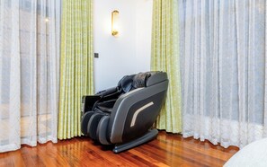 A massage chair in a room with wooden flooring and patterned curtains.