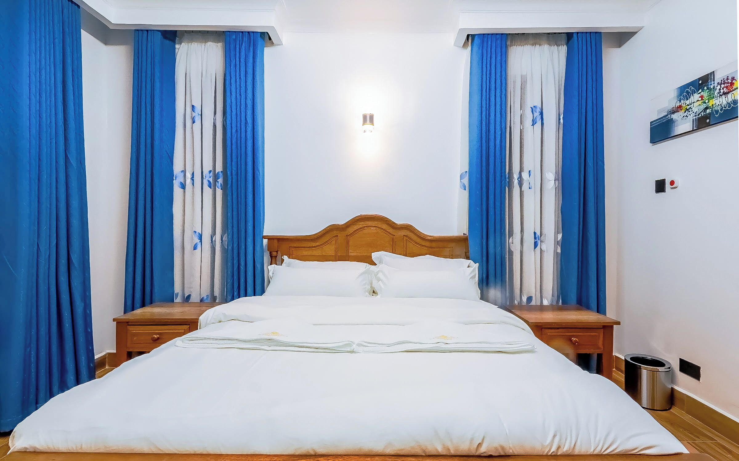 A hotel room with a wooden bed, white bedding, and blue curtains with floral patterns.