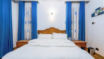 A hotel room with a wooden bed, white bedding, and blue curtains with floral patterns.