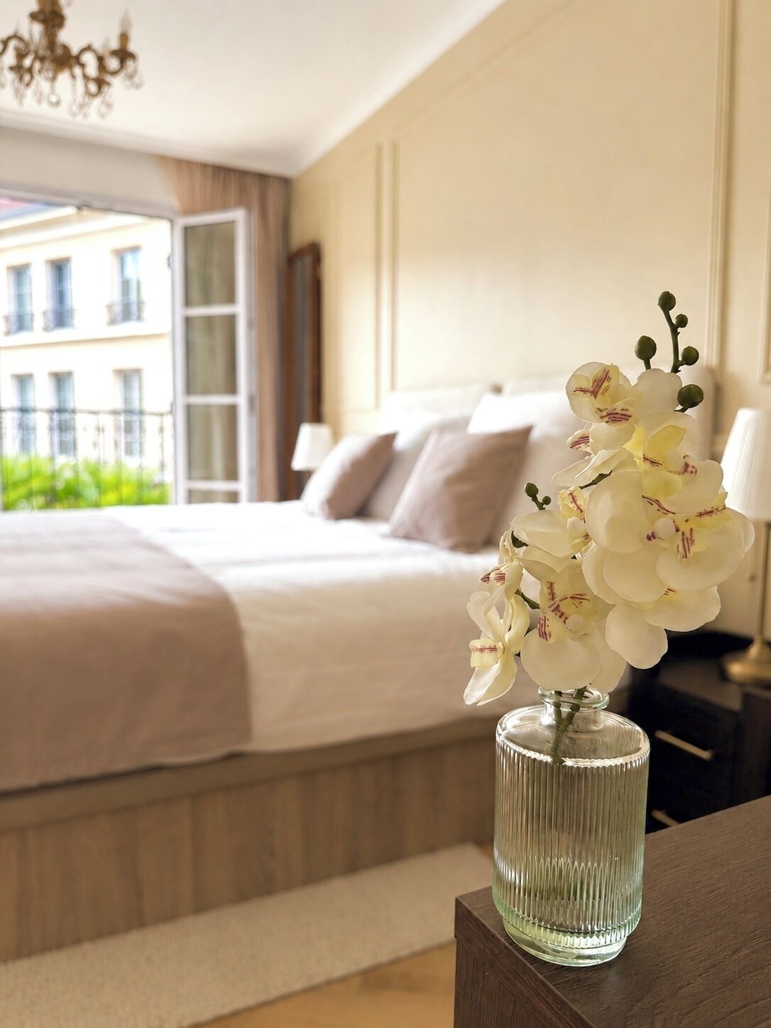 Quarto de hotel com uma cama, uma mesa de cabeceira, um vaso com flores e vista para prédios.