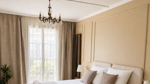 Een slaapkamer met een groot bed, een kroonluchter, een nachtkastje en een raam met gordijnen.