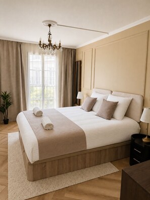 A bedroom with a large bed, a chandelier, a nightstand, and a window with curtains. - NEW - Haussmann-Style Appartment - 6 Guests - Disney & shopping (Serris)
