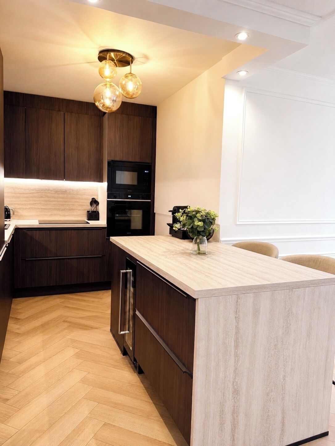 Een moderne keuken met donkere houten kastjes, een centraal eiland, een ingebouwde oven en een hanglamp.