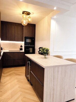 A modern kitchen with dark wood cabinets, a central island, a built-in oven, and a pendant light fixture. - NEW - Haussmann-Style Appartment - 6 Guests - Disney & shopping (Serris)