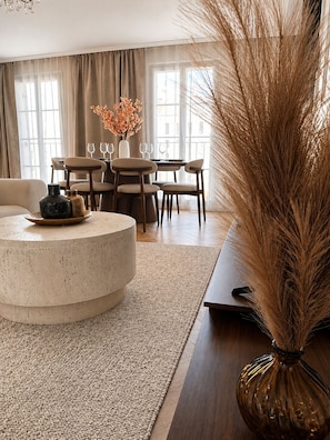 A modern living room with a round coffee table, a sofa, and a dining area with chairs and a table set for two. - NEW - Haussmann-Style Appartment - 6 Guests - Disney & shopping (Serris)